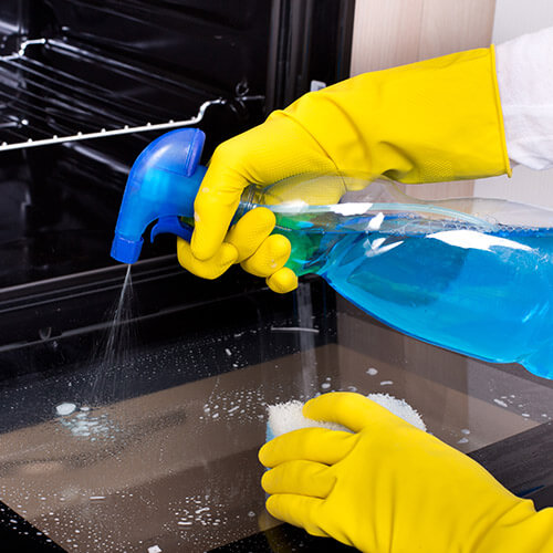 Hands In Rubber Gloves Spraying Solution On Oven Glass 