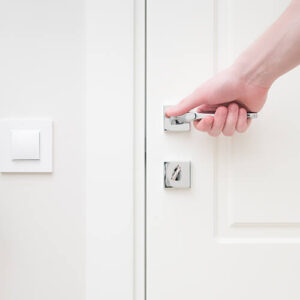 Hand Holding Door Knob With Light Switch Next To It