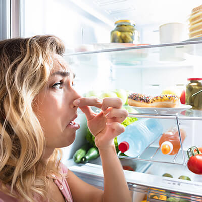 Woman Holding Her Nose By Fridge