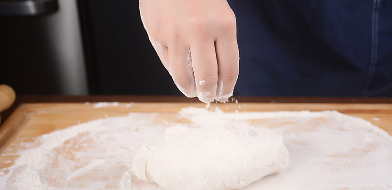 Close Up On Hand Adding Flour To Dough