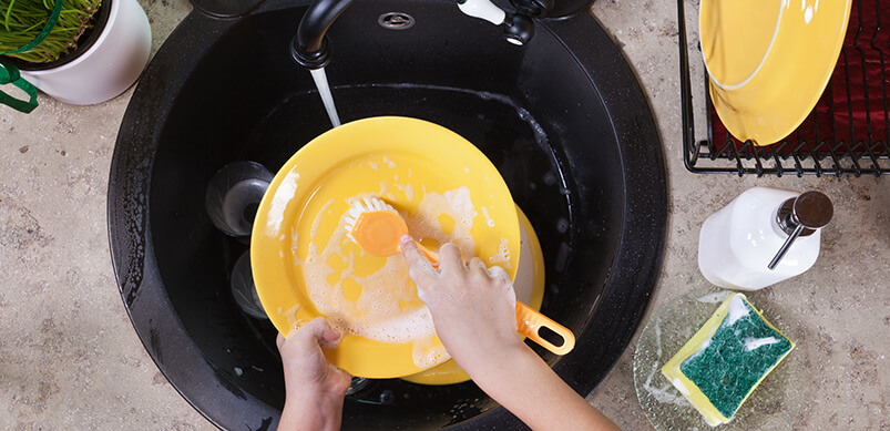 Hands Washing Yellow Plate In Black Sink