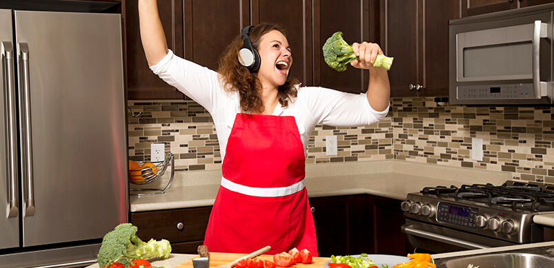 Woman Singing Into Broccoli In Kitchen 