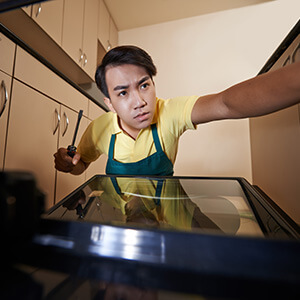 Man Looking Into Oven With Screwdriver