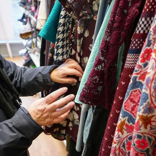 Woman Looking Through Clothes In Second Hand Shop