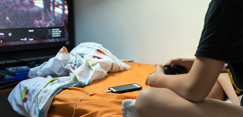 Teenager Playing Playstation With Phone Charging 