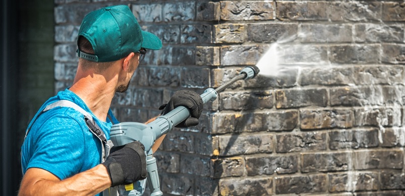 Man cleaning wall with pressure washer hose