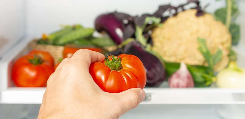 Hand putting tomato in fridge