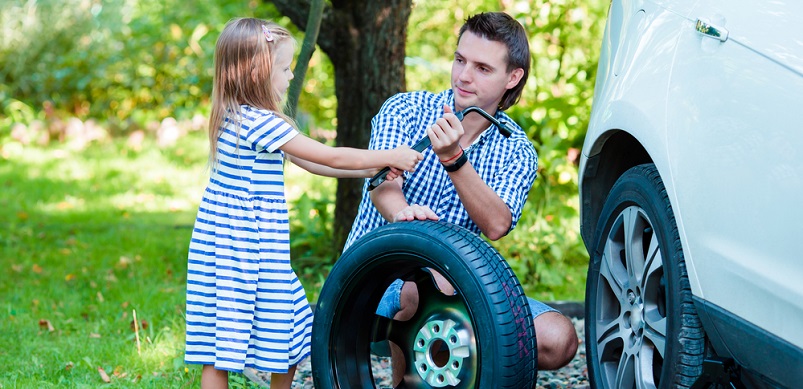 Little girl helping father change car tire