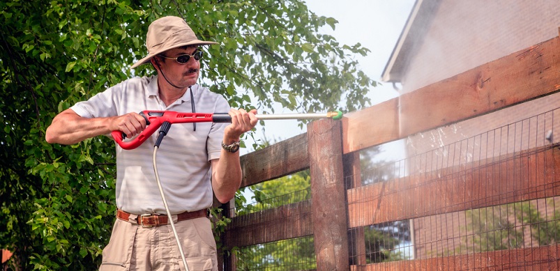 Man using pressure washer on fence